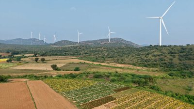 Wind turbines standing next to farmland in the sunshine.