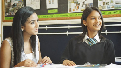 A student and teacher sitting together at a desk, looking at school work.