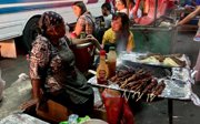 Two women preparing grilled meat at a traditional street market.