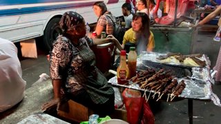 Two women preparing grilled meat at a traditional street market.