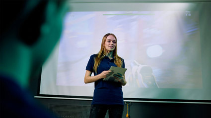 A person standing in front of a projection screen presenting to an audience.
