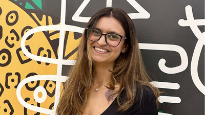 Portrait photo of Kinnari Saraiya against a colourful background with abstract shapes.