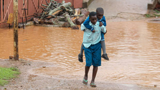 Adult carrying child on their back across flood water