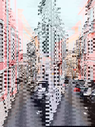 A road looking down into a bay, with pink houses and cars parked