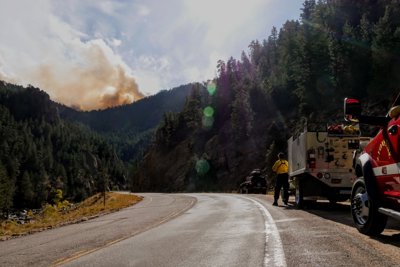 Trucks drive on a road which winds through a mountainous forest.