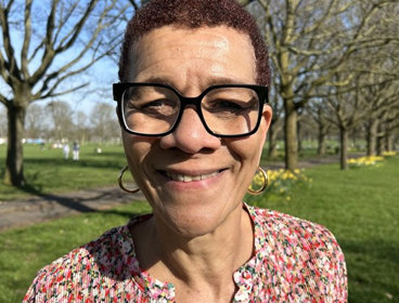 Person wearing black glasses and a patterened shirt against a backdrop of a park.