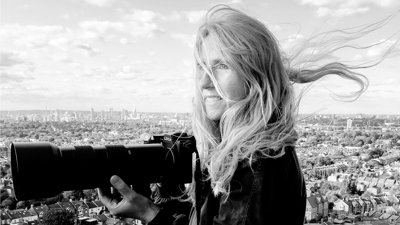 Black and white portrait photograph of Britta Jaschinski holding a Leica camera with a big lens.