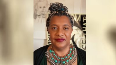 Heashot of person with braided hair wearing large colourful necklace. 