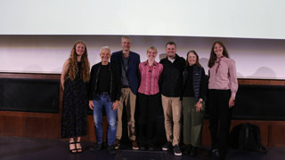 Paul Rose standing alongside six other speakers on the Ondaatje Theatre stage.