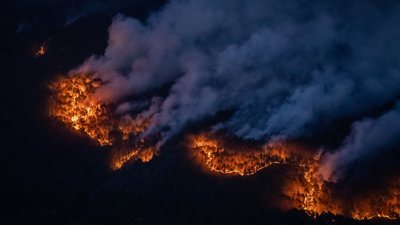 Wildfire at night with large plumes of smoke as seen from above.