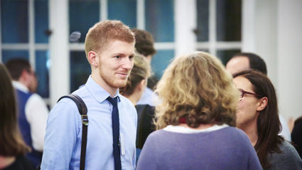Person in a blue shirt and tie talking to two other people.