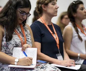 A person writing in a notebook, seated next to two other conference delegates.