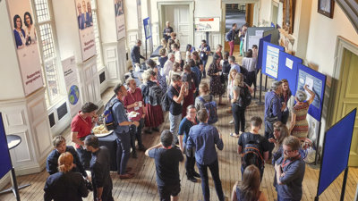 A group of people wearing lanyards in a stately Main Hall. The room features display boards and posters.