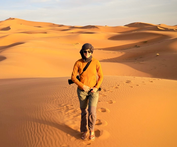 Person with camera wearing orange jacket in the middle of an sandy orange Morocco desert.