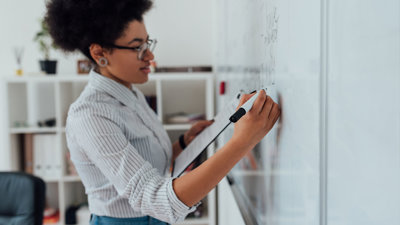 A teacher holding notes writing something on a whiteboard.