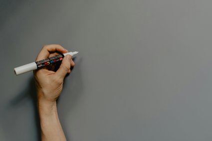 A hand holding a white marker pen and preparing to draw.