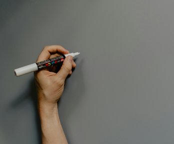 A hand holding a white marker pen and preparing to draw.