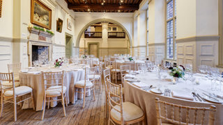 Round dinner tables with neutral linen set-up in a grand main hall for a wedding.