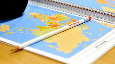 A page showing a world map. A pencil laying on it says 'www.rgs.org'