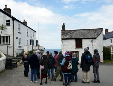 A tour group listening to the leader speaking in front of white, traditional seaside cottages.