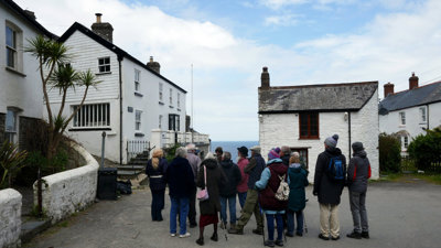 A tour group listening to the leader speaking in front of white, traditional seaside cottages.