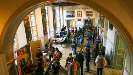 A large gathering of people networking in a stately main hall, as seen from above.