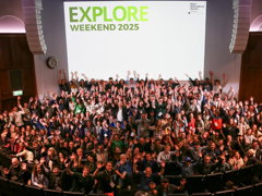 Explore delegates waving their hands and smiling at camera during group photo in the Ondaatje Theatre