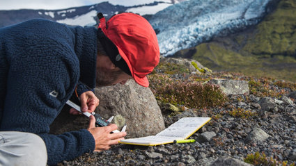 Person measuring the size of a mark on the side of a rock in a rocky landscape.