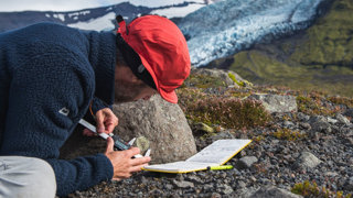 Person measuring the size of a mark on the side of a rock in a rocky landscape.