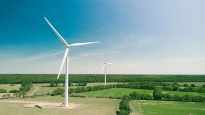 Two wind turbines in open fields with a clear sky. 