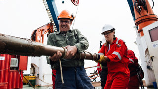 Two people on a ship pulling a wooden beam.