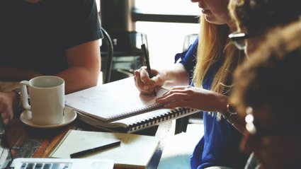 Group of people sat around a table with one person writing notes in a notebook