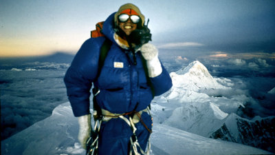 Mountain climber wearing blue jacket on top of snow-capped mountain.