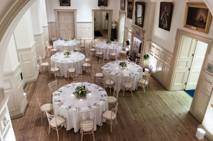 Five round tables with wooden chairs and white linen setup for a dinner in the Main Hall.