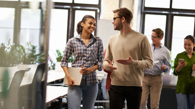 Two coworkers talking and smiling while walking down a modern office.