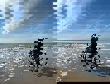 An empty wheelerchair on a sandy beach, facing towards the sea