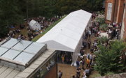 A large white marquee in the garden of a building. There are hundreds of people filling it and outside too.