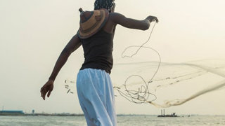 Person throwing a fishing net into water from a boat.