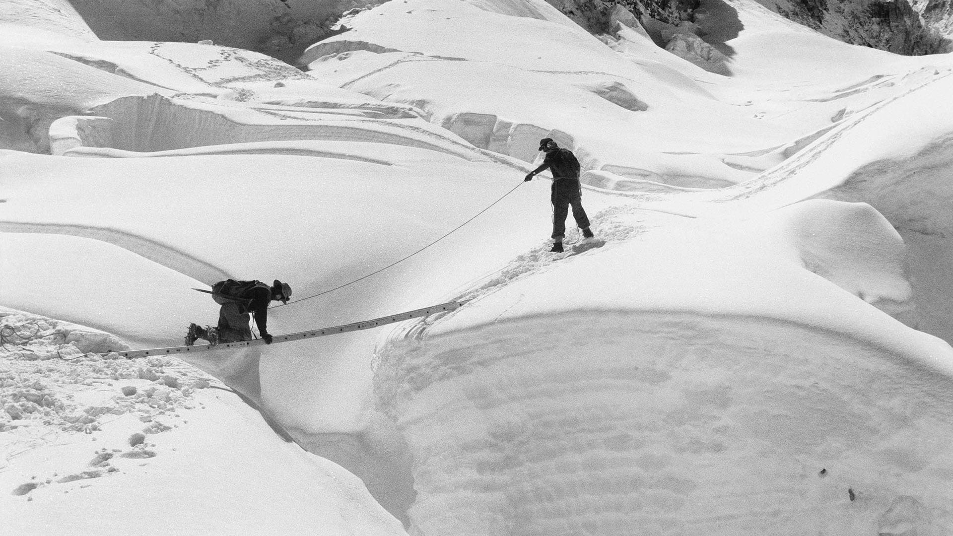 Edmund Hillary assists Tenzing Norgay crossing a crevasse by ladder.