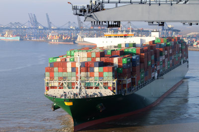 Container ship showing coloured shipping containers piled up, with cranes in the background