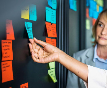 Colleagues placing colourful sticky notes on a glass board.