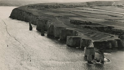 Black and white aerial photograph of eroding coastline.