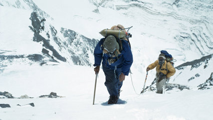 Two mountaineers in full winter tracking gear walking a snow covered mountain.