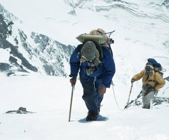 Two mountaineers in full winter tracking gear walking a snow covered mountain.