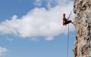 Woman in rock climbing gear ascending a rock.