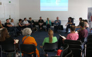 Group of people sit in a circle at a conference, they are sitting on black chairs.