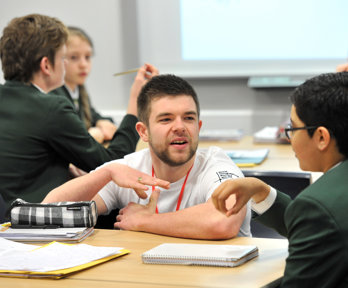 A male geography ambassador crouching down next to a male student, talking to them about geography