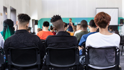 Teenagers sit in a hall listening to a presenter speak