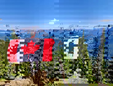 Man standing overlooking a mountain view, holding a Canadian flag