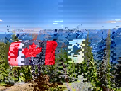 Man standing overlooking a mountain view, holding a Canadian flag